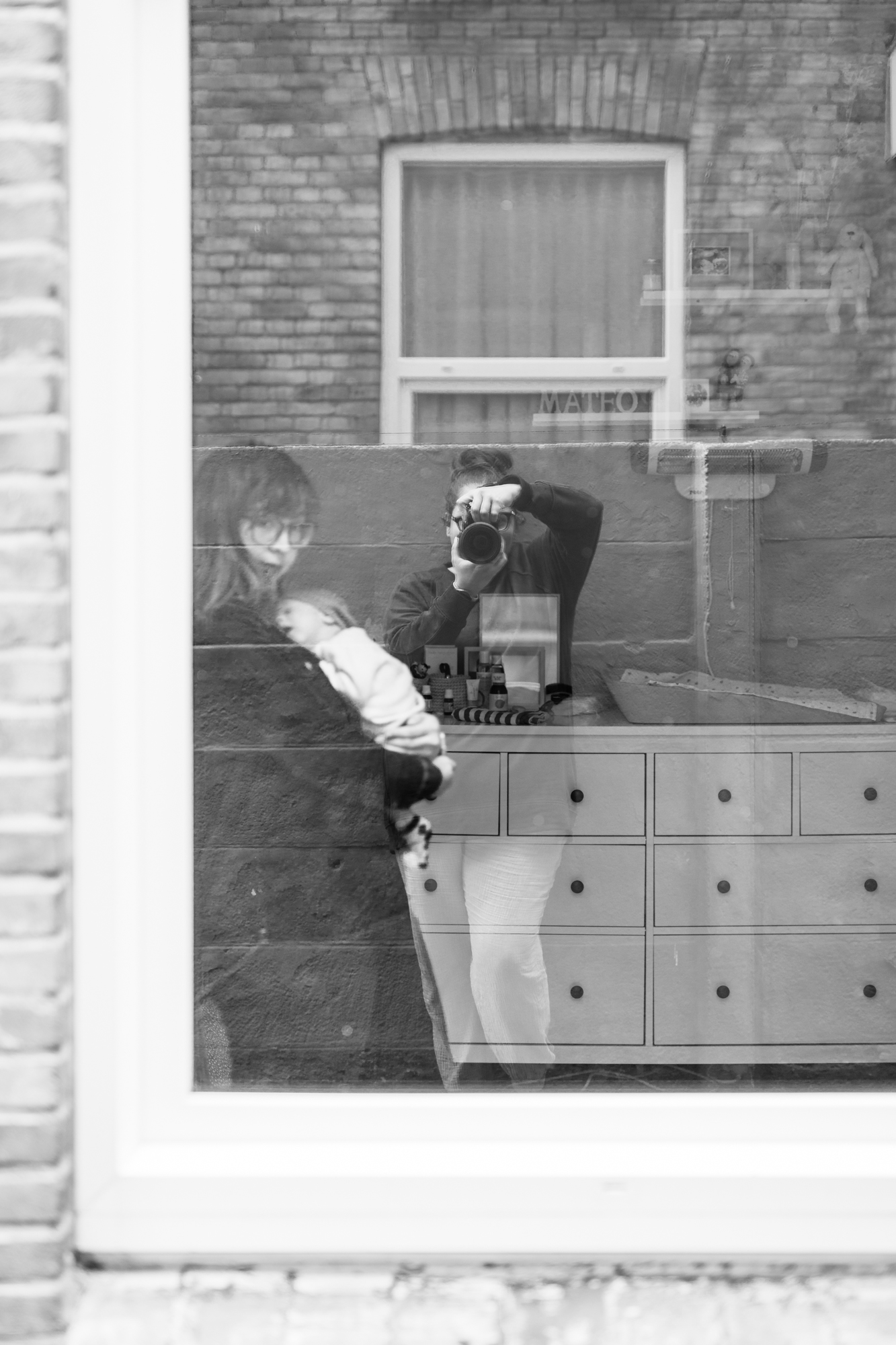 Reflection of photographer documenting home session with newborn and family, black and white photography
