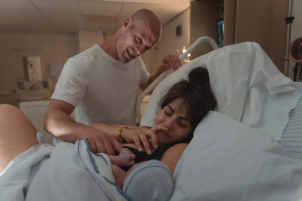 Father touching his newborn daughter on her mother's chest in the delivery room in Arnhem