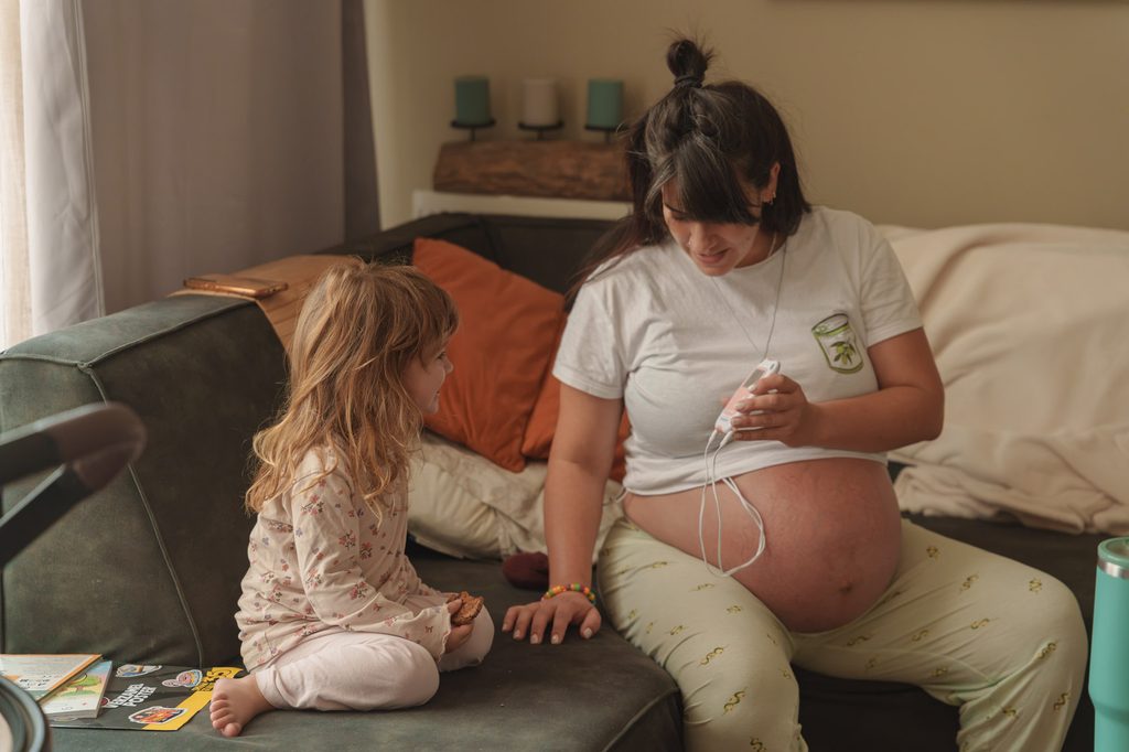 Big sister sitting with her pregnant mother on the sofa before her baby sister is born
