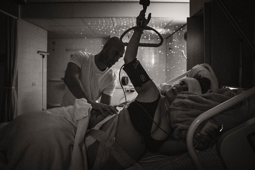 Black and white photo of a mother labouring in the hospital with her partner by her side